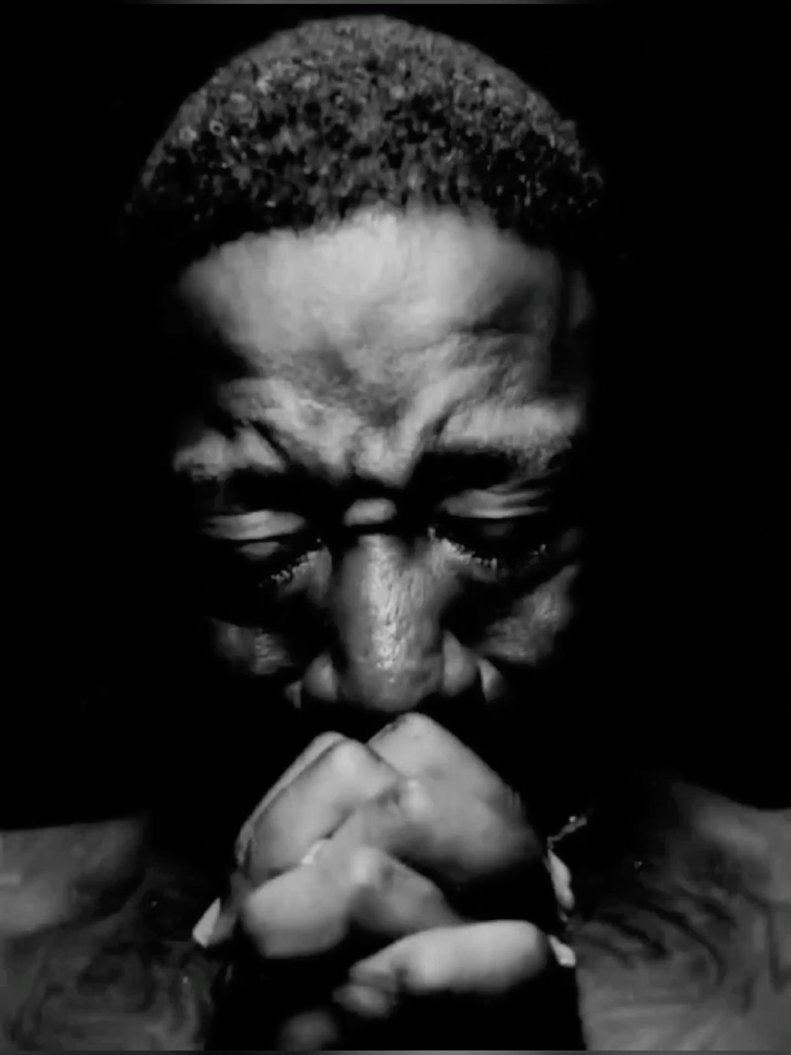 Black-and-white shot of a man with clasped hands and eyes shut, deep in it