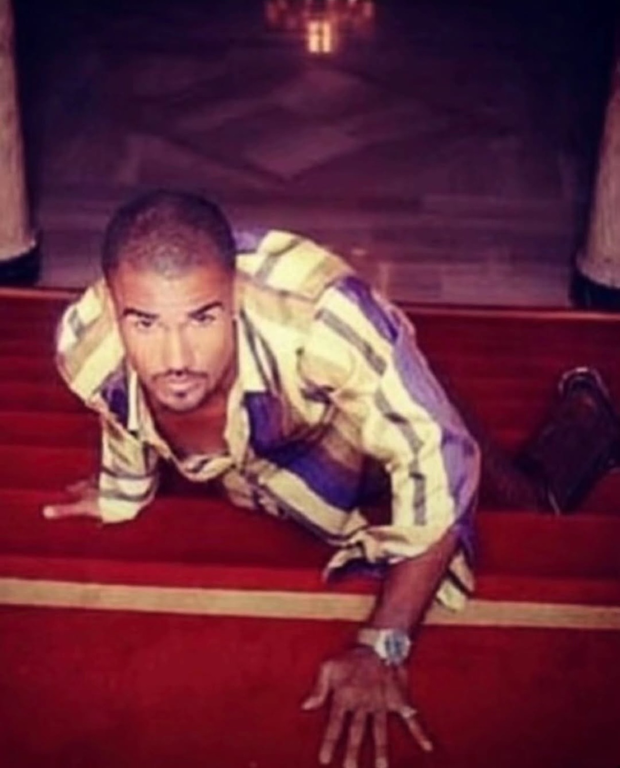 Man crawling up red carpeted stairs staring seductively at the camera