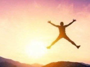 Silhouette leaping into a pink sunset sky with both arms thrown wide