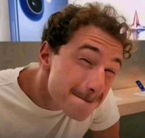 Curly-haired guy resting his face in his hand with a pained, cringe-worthy expression in an Apple Store