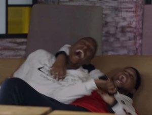Two guys on a couch completely losing it, one sprawled over the other in hysterics
