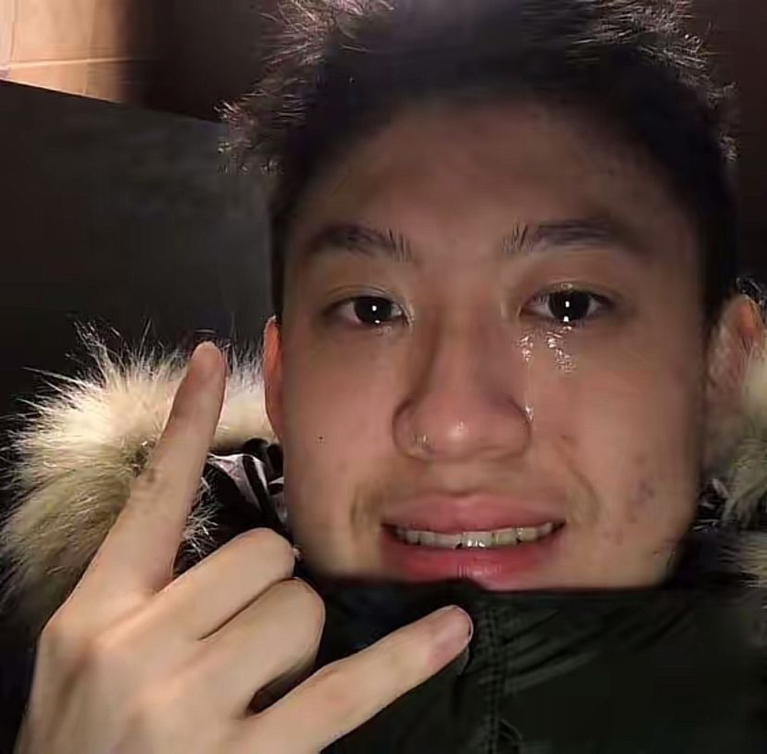 Young man tearing up while throwing a finger-gun gesture in a fur-lined hood