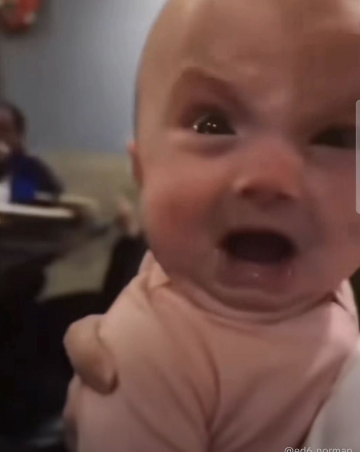 Red-faced baby absolutely losing it while being held up, deeply upset about something