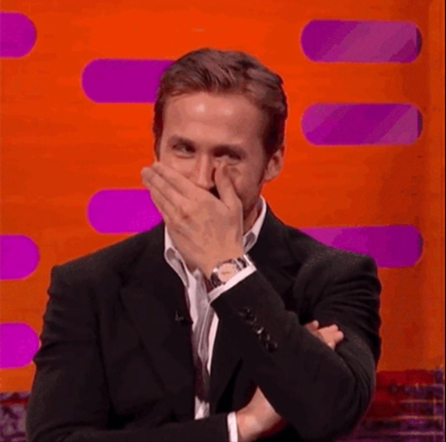 Ryan Gosling covering his face with his hand, shoulders shaking with laughter on a talk show
