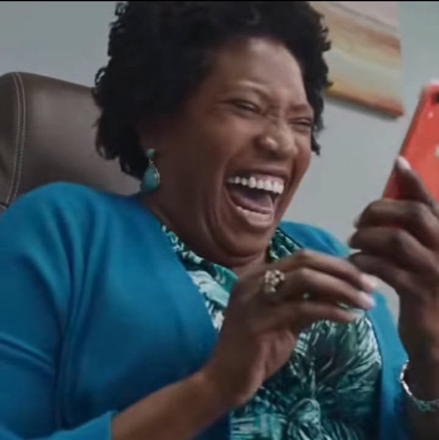 Woman in teal laughing hysterically at her phone, absolutely losing it