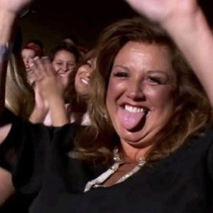 Woman in black sticking her tongue out and cheering with a crowd behind her