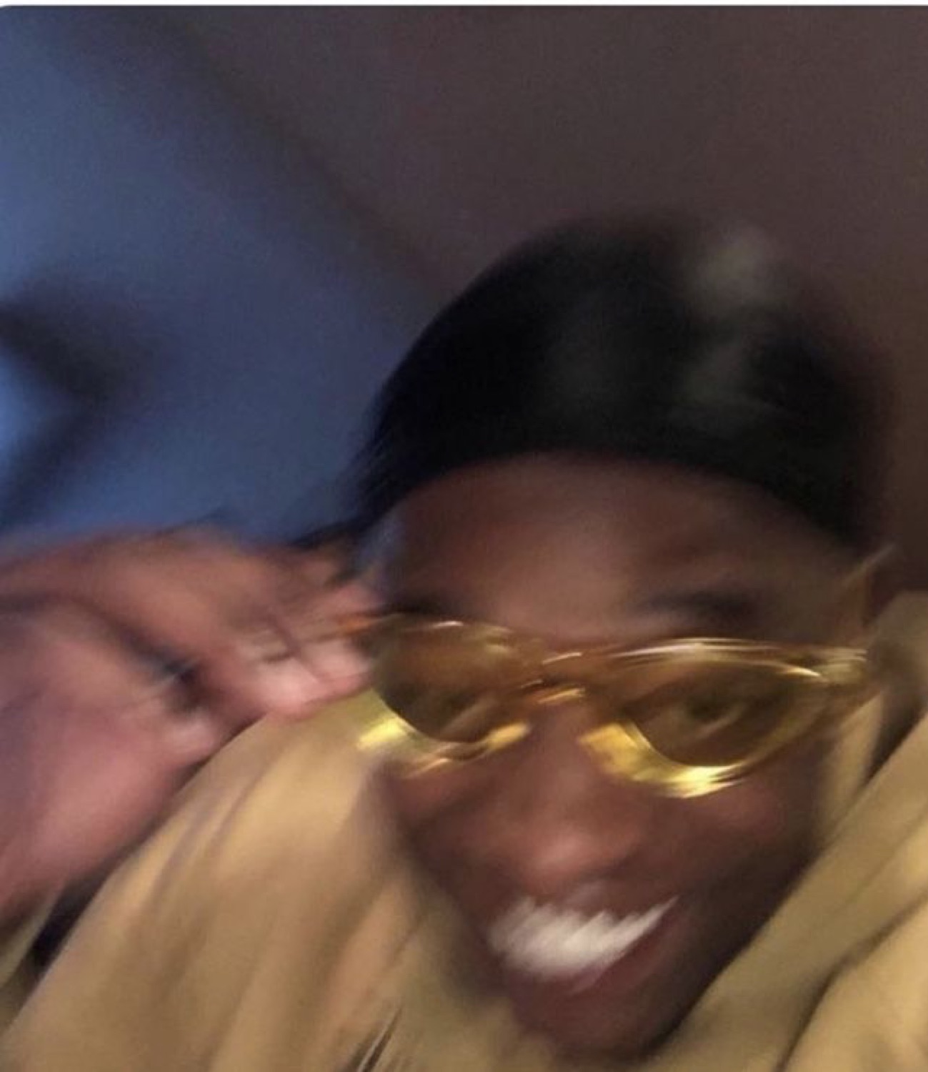 Blurry motion selfie of someone grinning wide in gold-frame sunglasses and a beanie