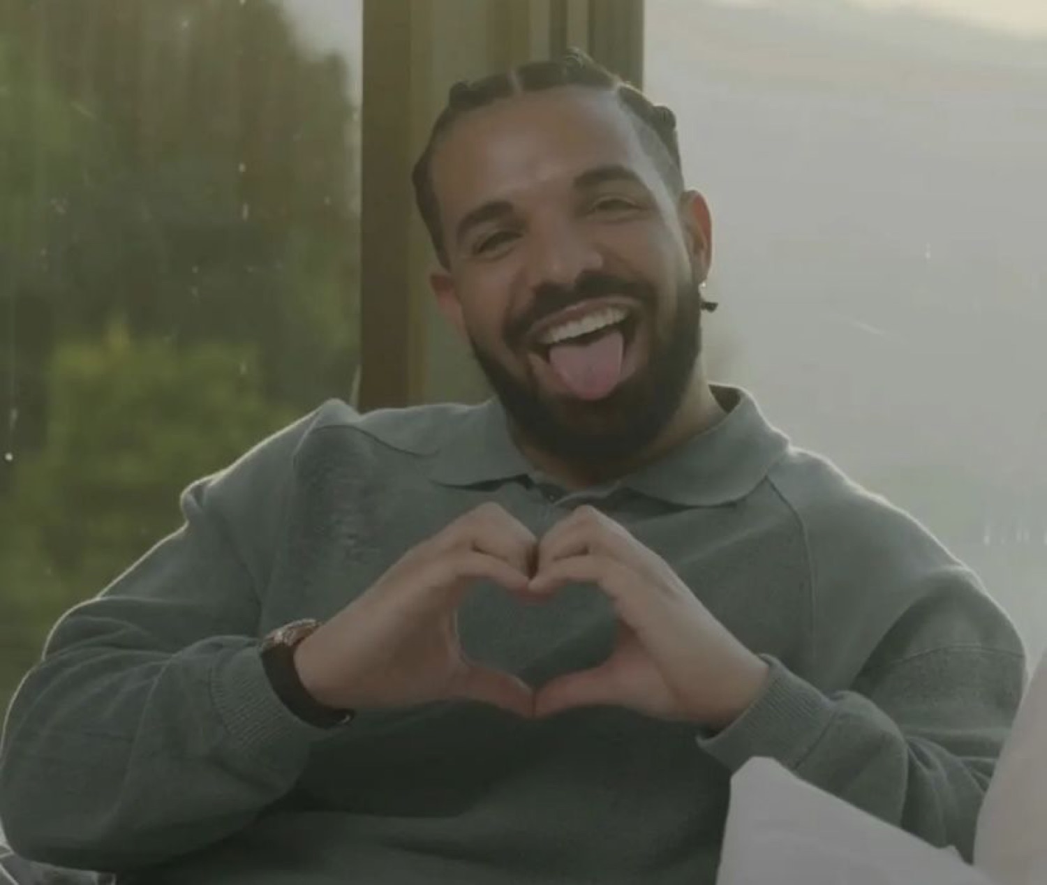 Drake making heart hands with his tongue out and a big goofy grin