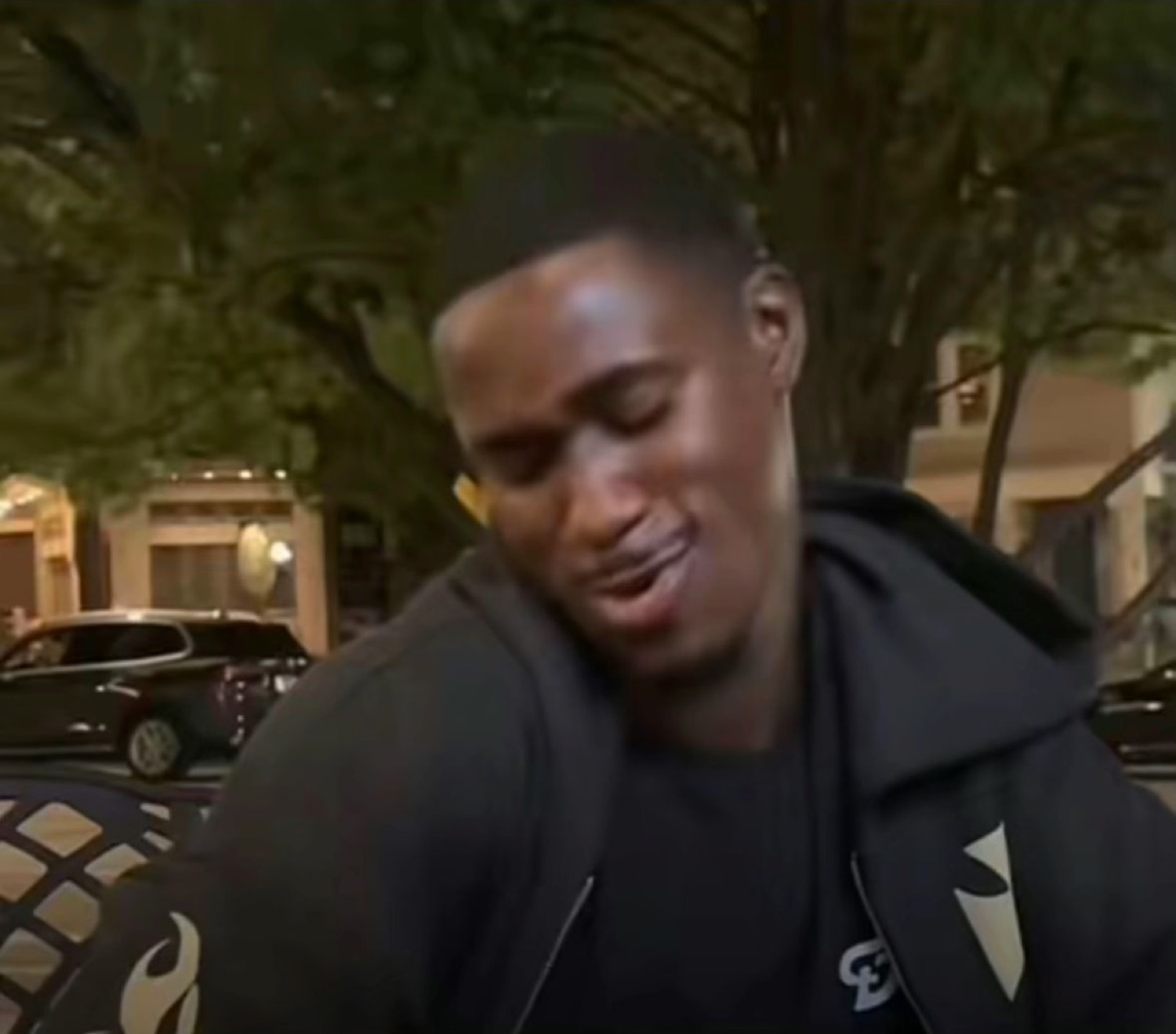 Young man in a black hoodie looking down with a pained, emotional expression outdoors at night
