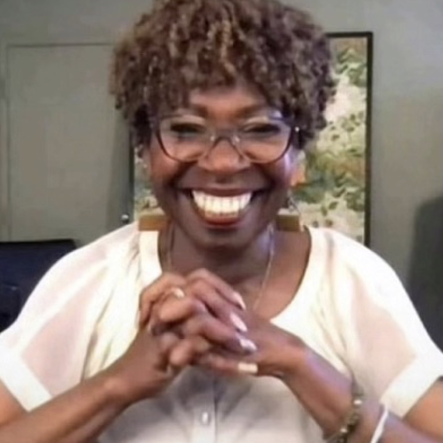 Woman in glasses beaming with hands clasped, absolutely delighted