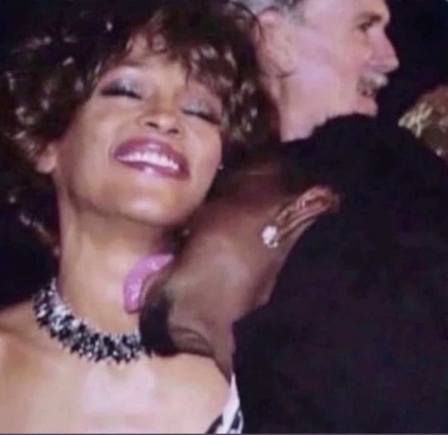 Woman in a glittery necklace laughing with joy, head tilted back at a glamorous event