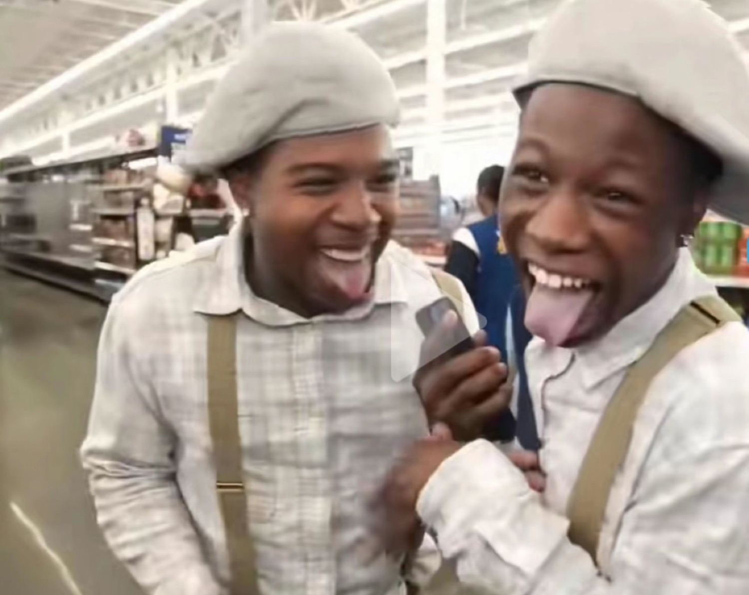 Two guys in matching berets cracking up with their tongues out in a supermarket aisle