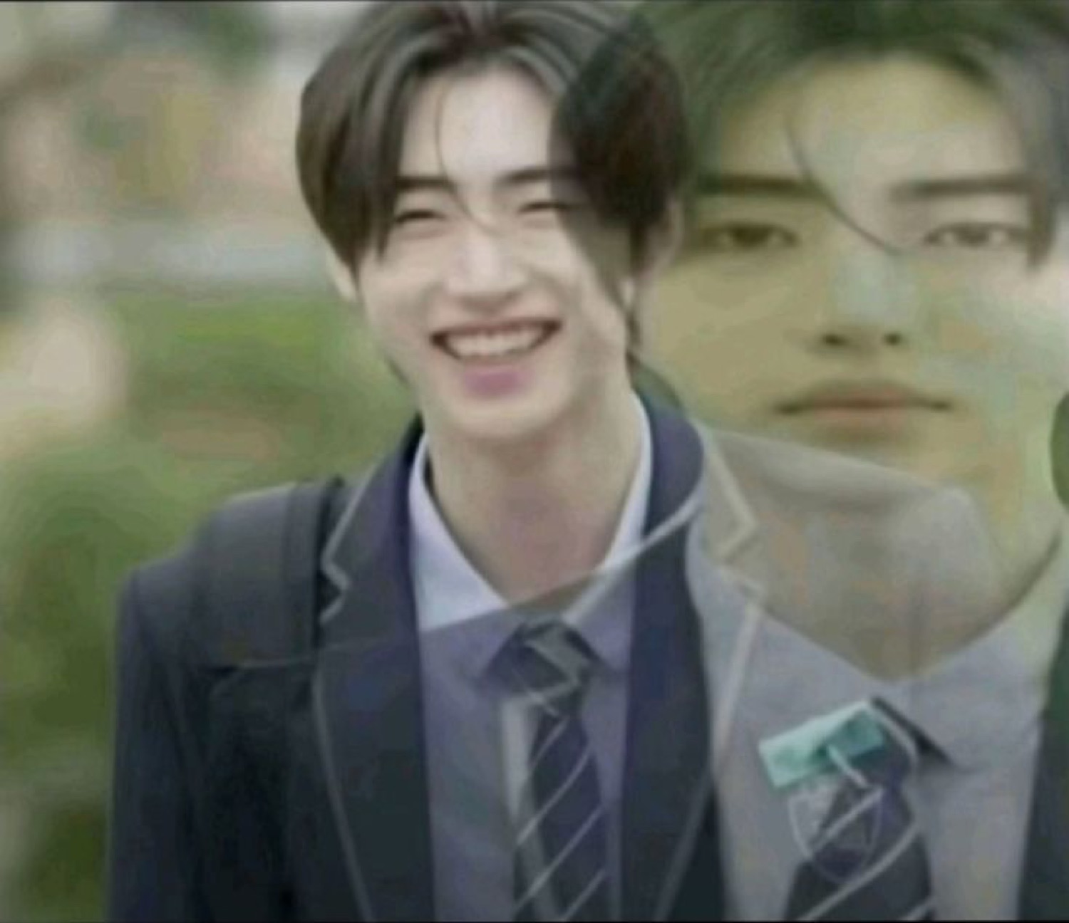 Young man in school blazer flashing a wide smug grin, with a ghost reflection behind him