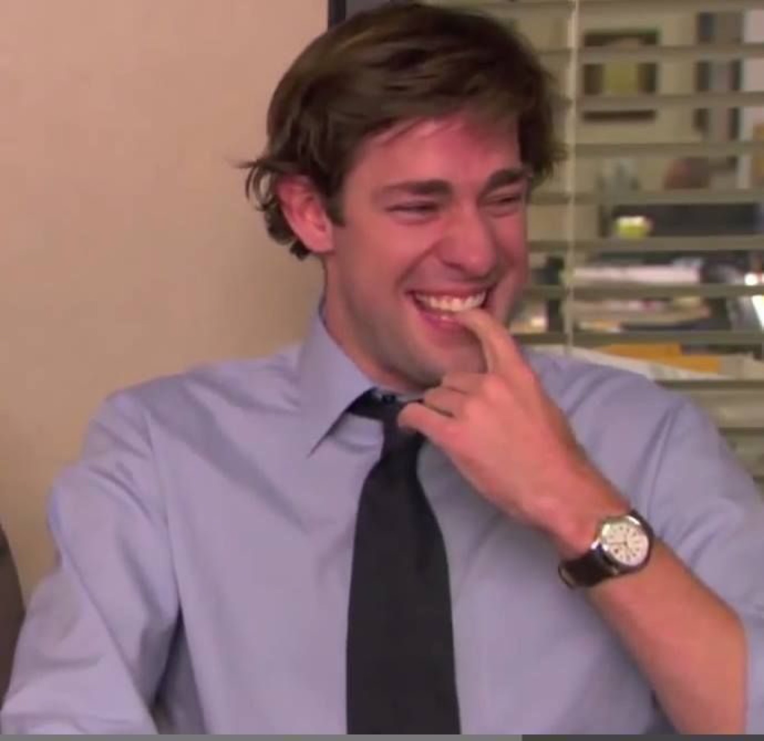 Office guy in a shirt and tie cracking up with a finger at his mouth