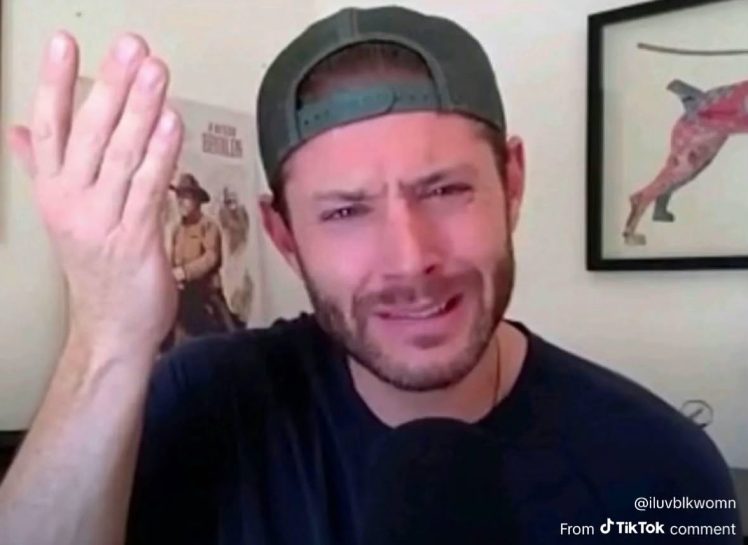 Man in a baseball cap crying with one hand raised, overcome with emotion on a video call