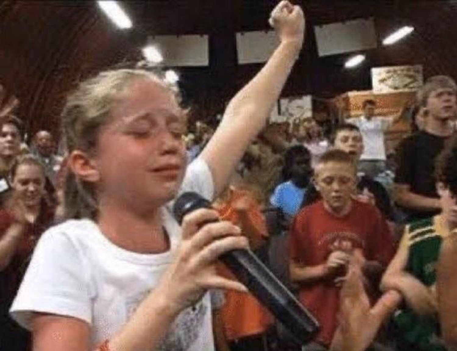 Girl at a mic sobbing with her fist thrown in the air in the middle of a crowd