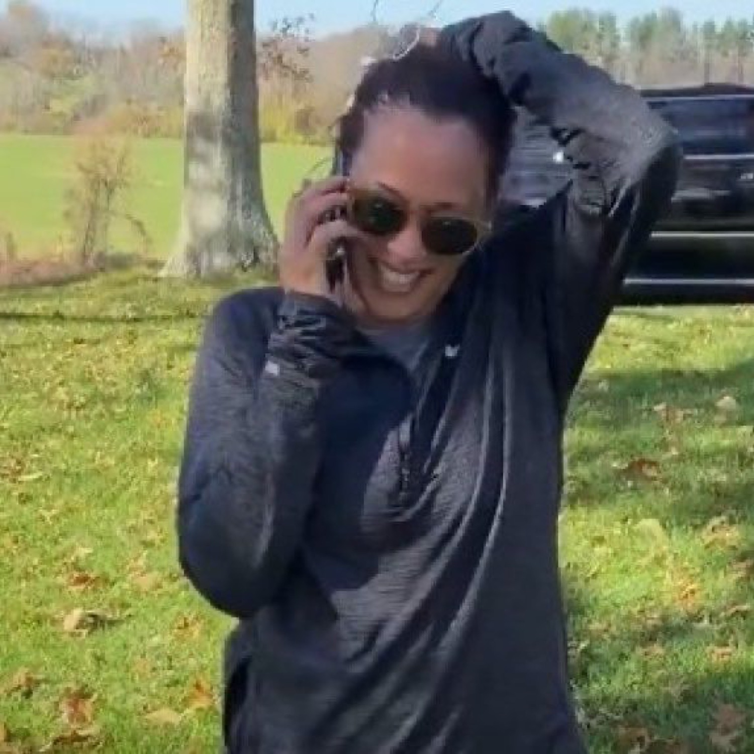 Woman in sunglasses laughing on a phone call outdoors, totally losing it