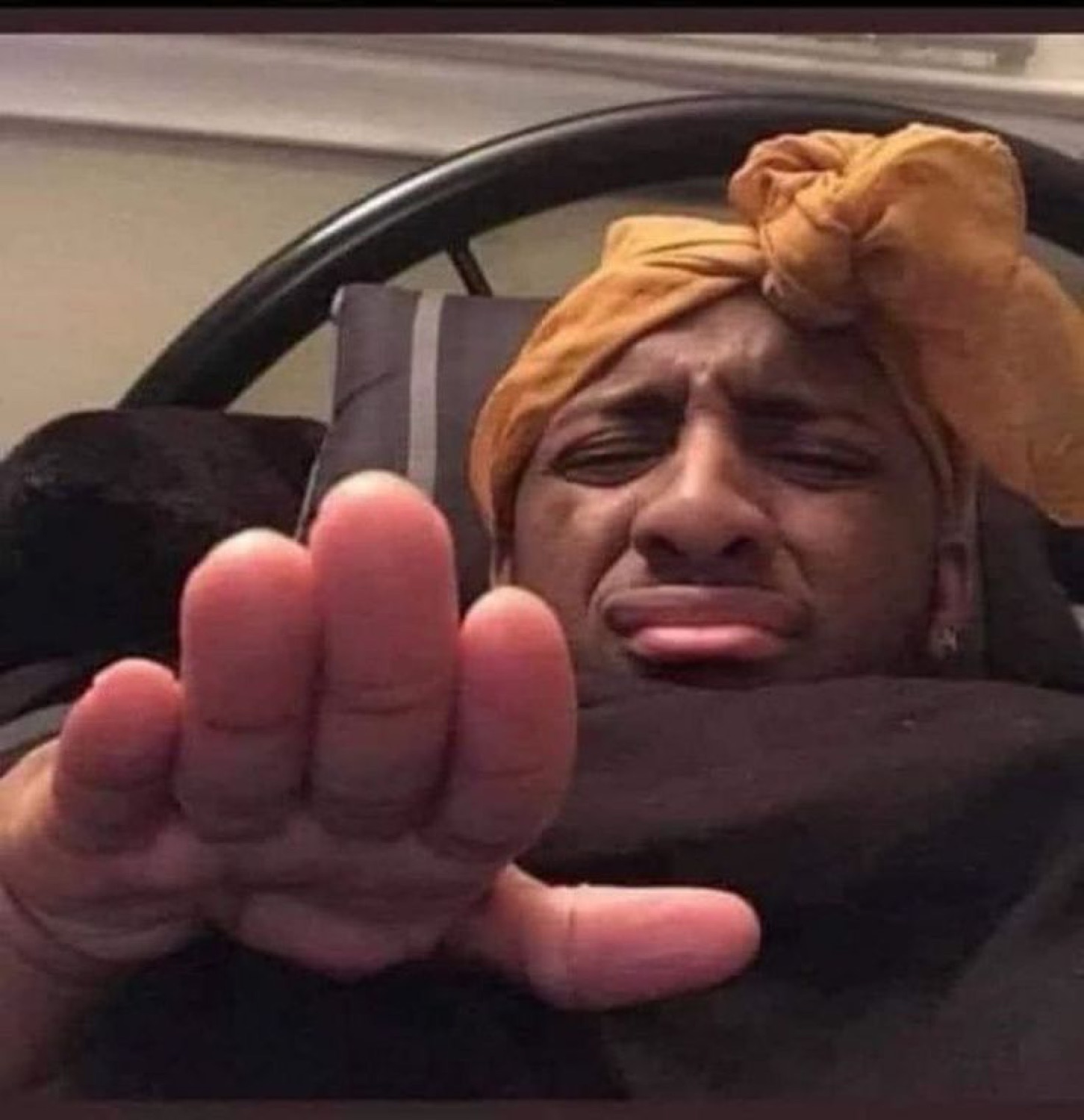Person in a yellow head wrap crying and reaching a hand out toward the camera in a car