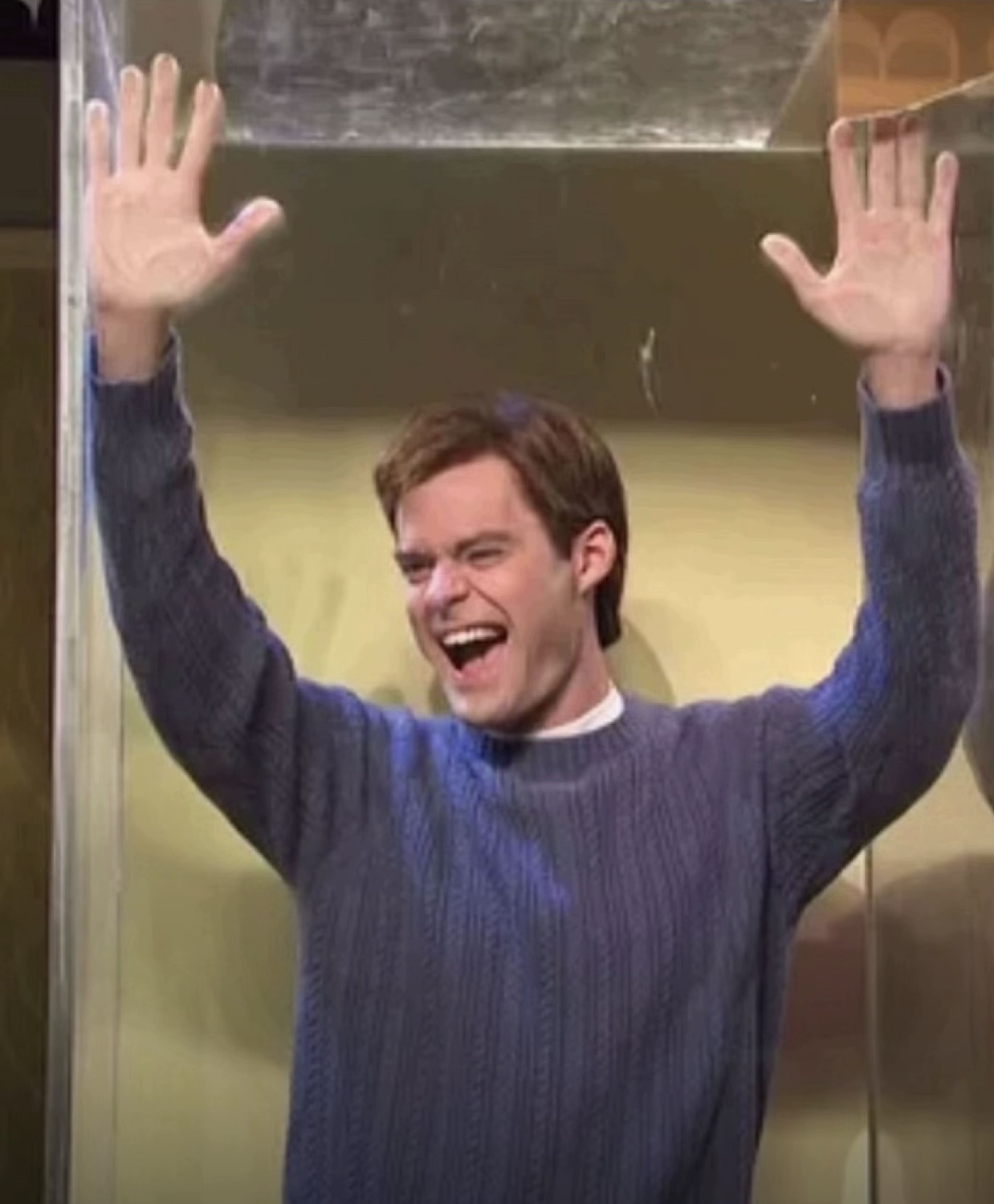 Man in a blue sweater bursting through a glass door with arms raised and a huge grin