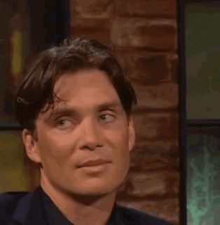 Cillian Murphy on a talk show glancing sideways with a tight, unimpressed smirk