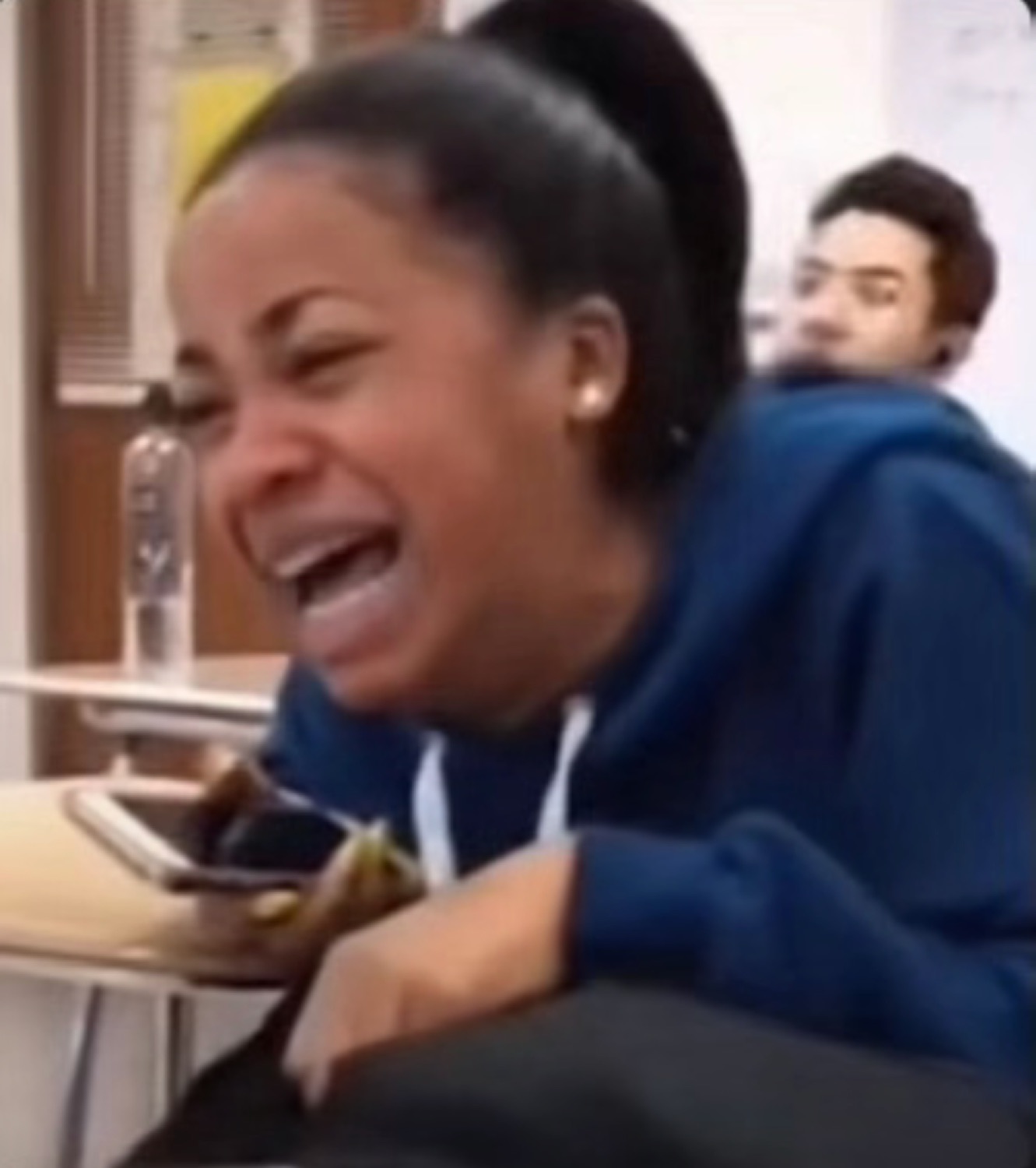Girl in a classroom doubled over a desk laughing so hard she's crying