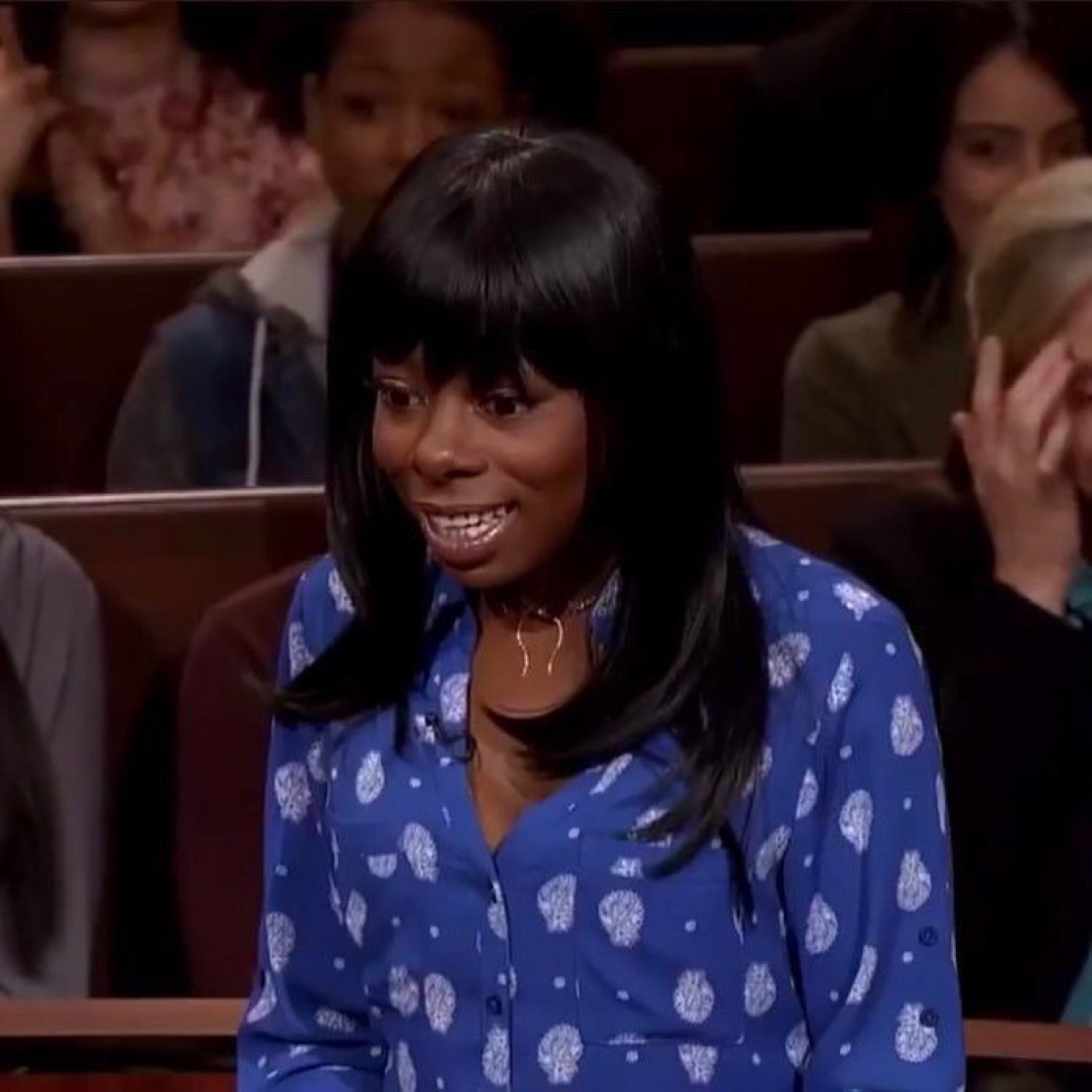 Woman in a courtroom show giving a wide, tense, nervous grimace-smile