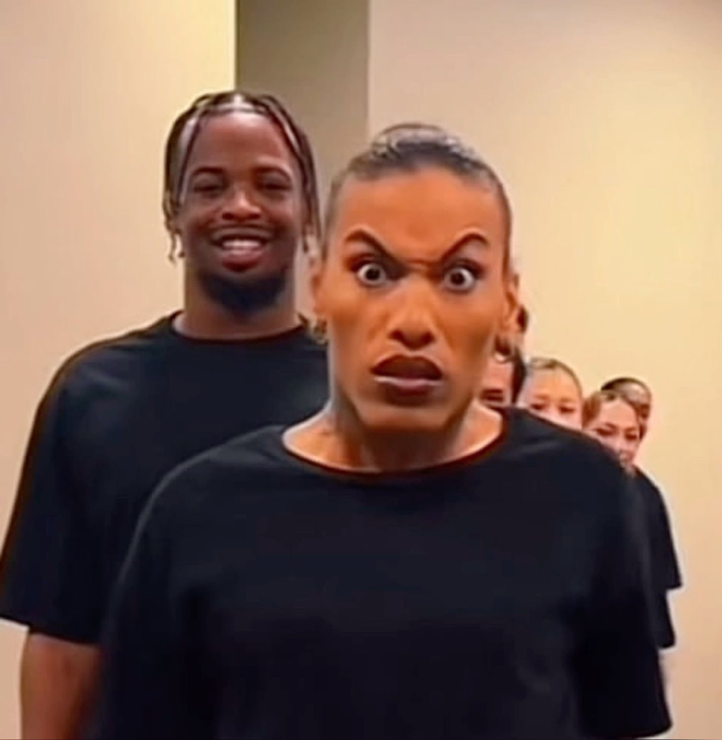 Woman in front pulling a bug-eyed furious face while a man grins behind her