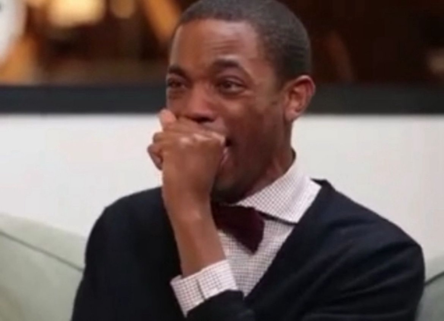 Man covering his mouth with a fist, wincing between shock and a laugh