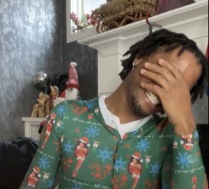Guy in a Christmas onesie covering his face while laughing uncontrollably