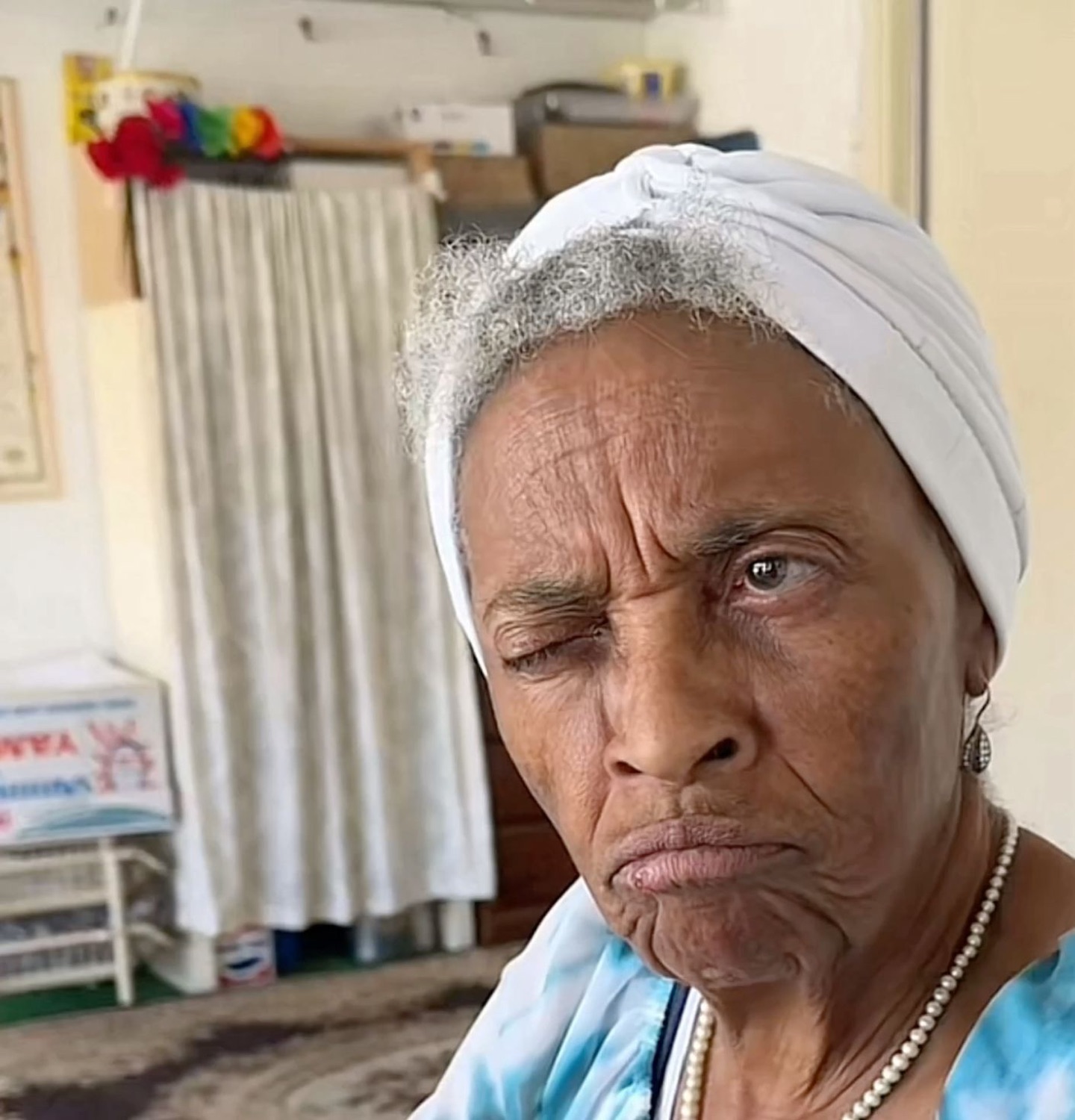 Elderly woman in a headwrap giving a squinting, unimpressed side-eye