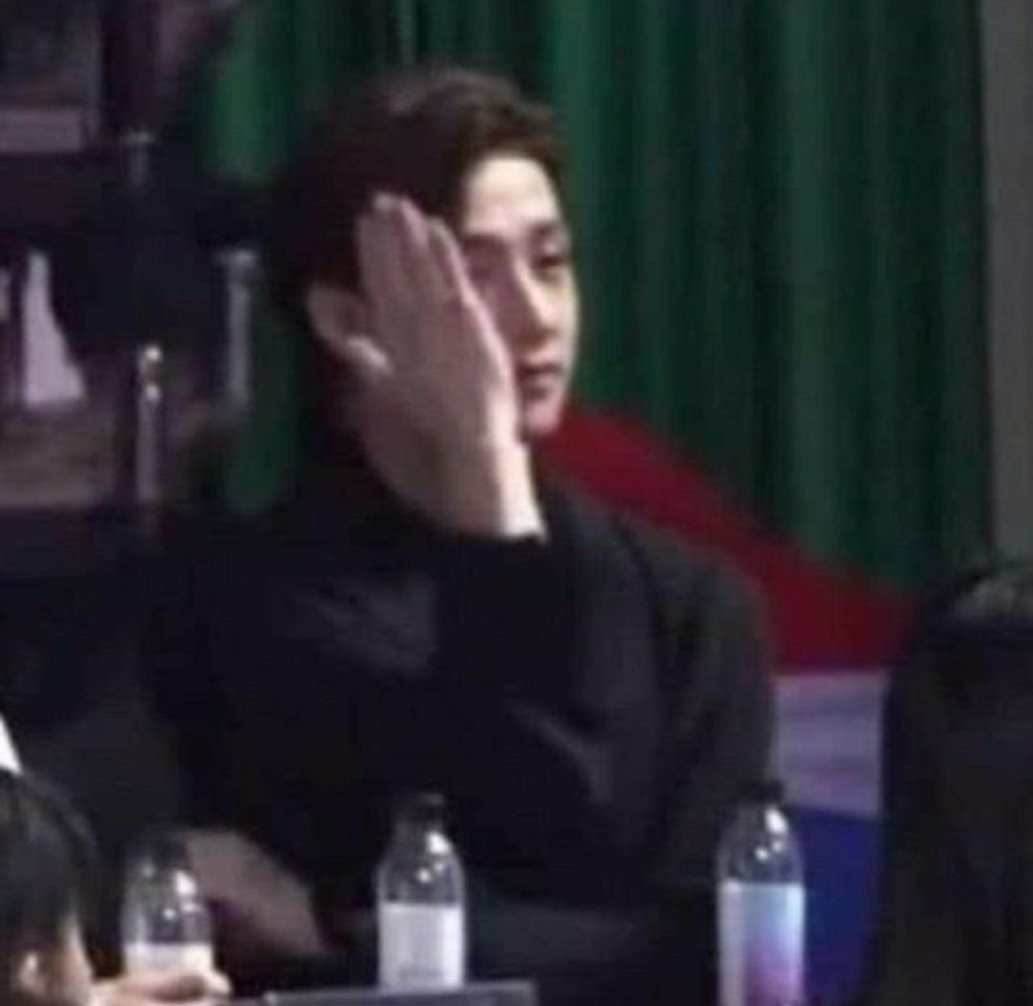 Young man in all black resting his face in his hand with a blank stare