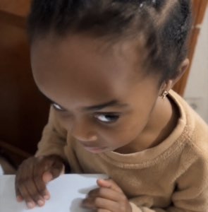 Toddler leaning on a table giving an intense side-eye with a scheming look