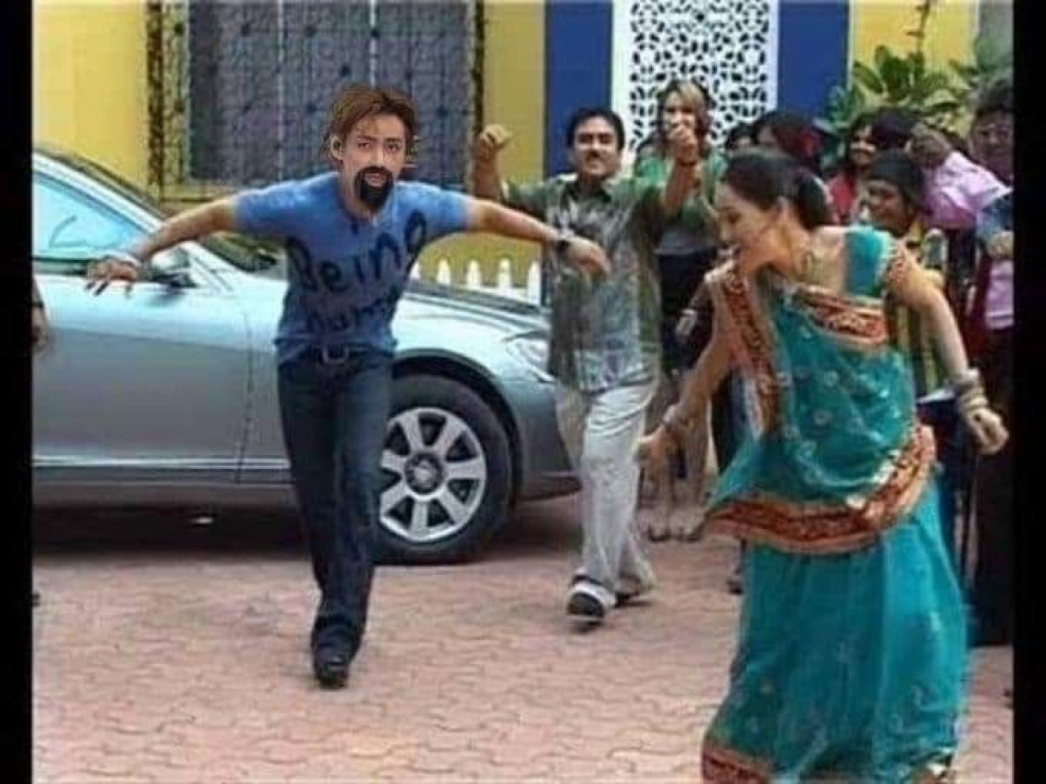 Man in jeans dancing wildly in the street next to women in saris