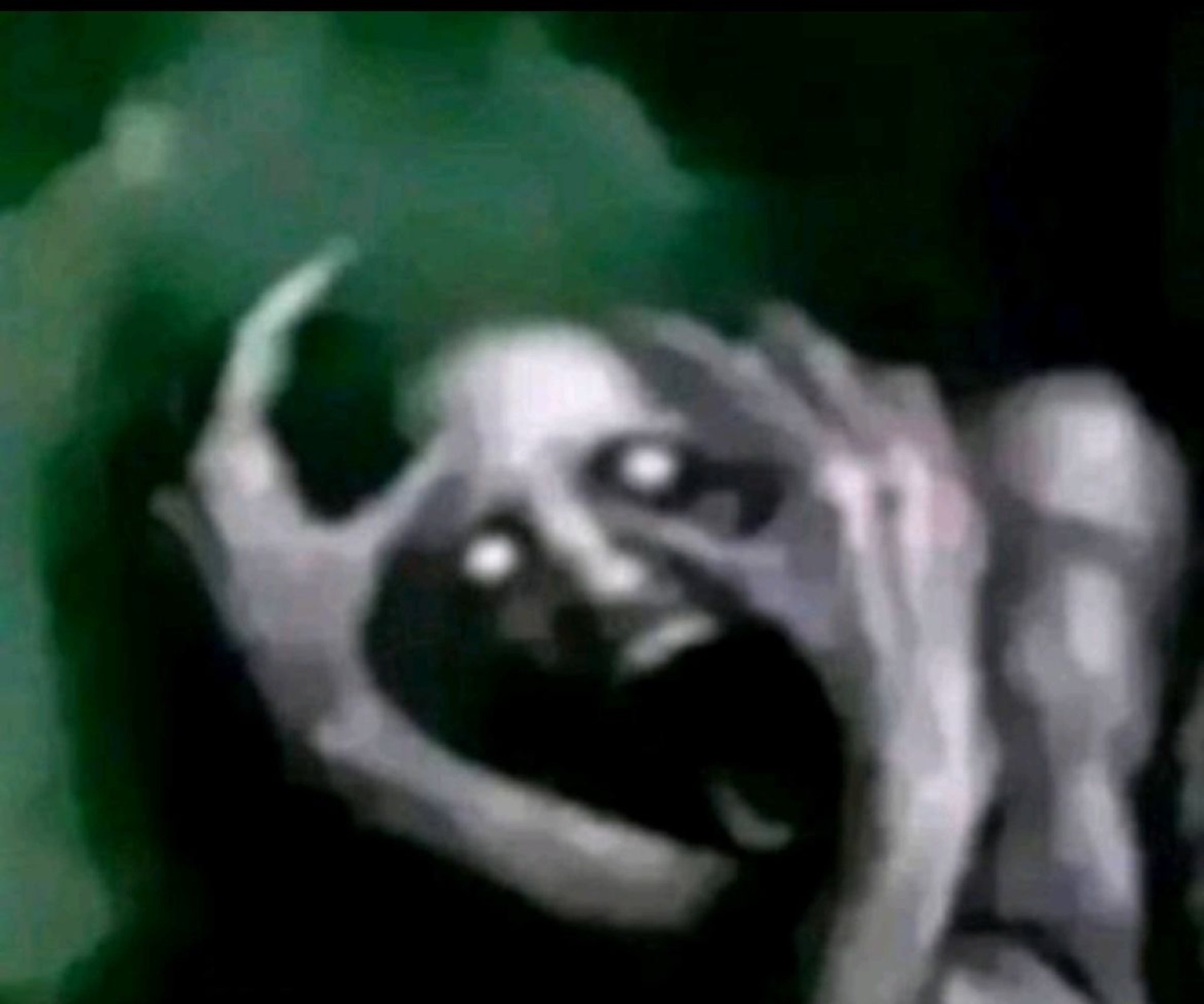 Grainy dark image of a ghoulish figure with hollow white eyes and a screaming face