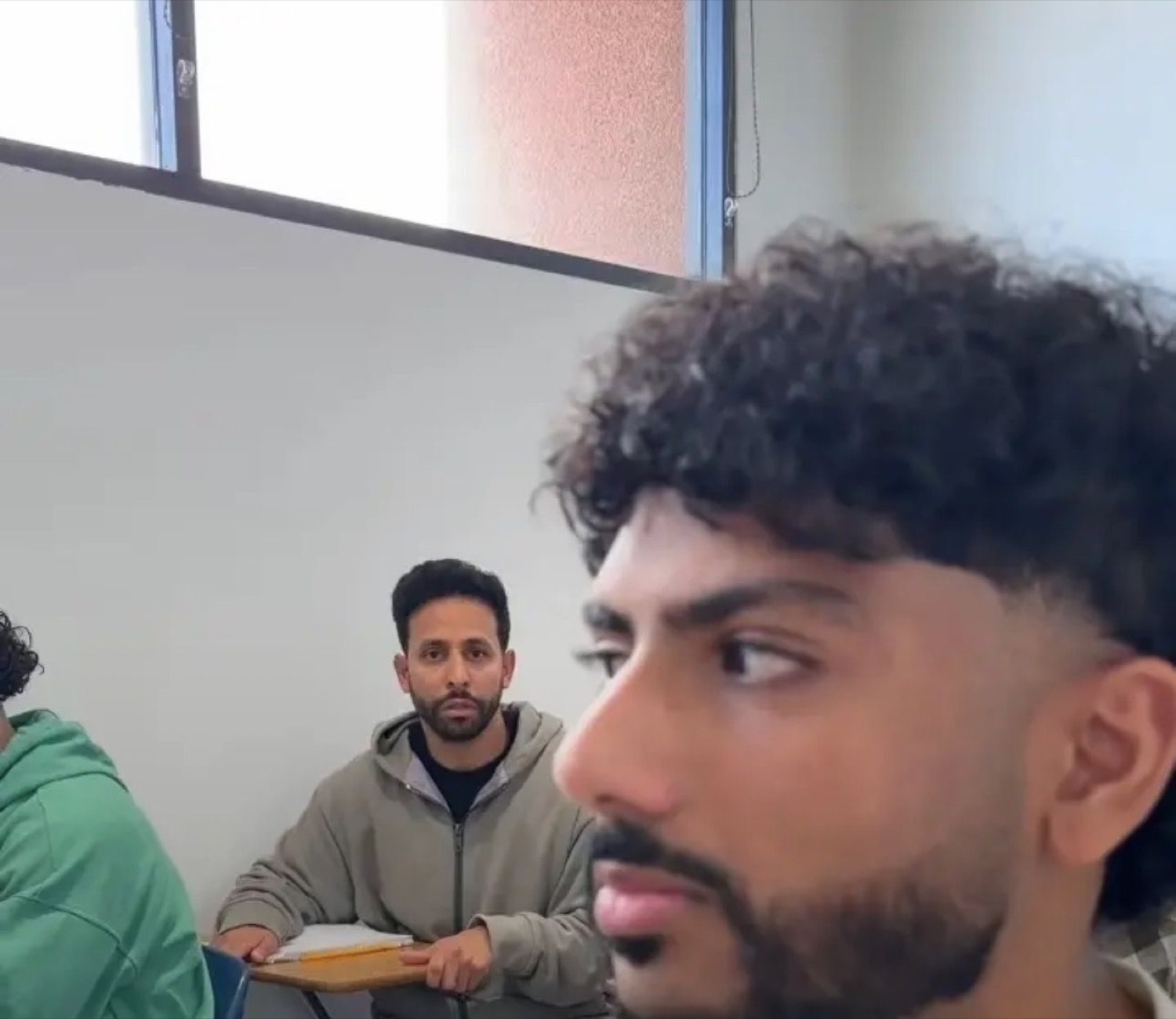 Two guys in a classroom, one in the foreground side-eyeing hard while another stares from behind