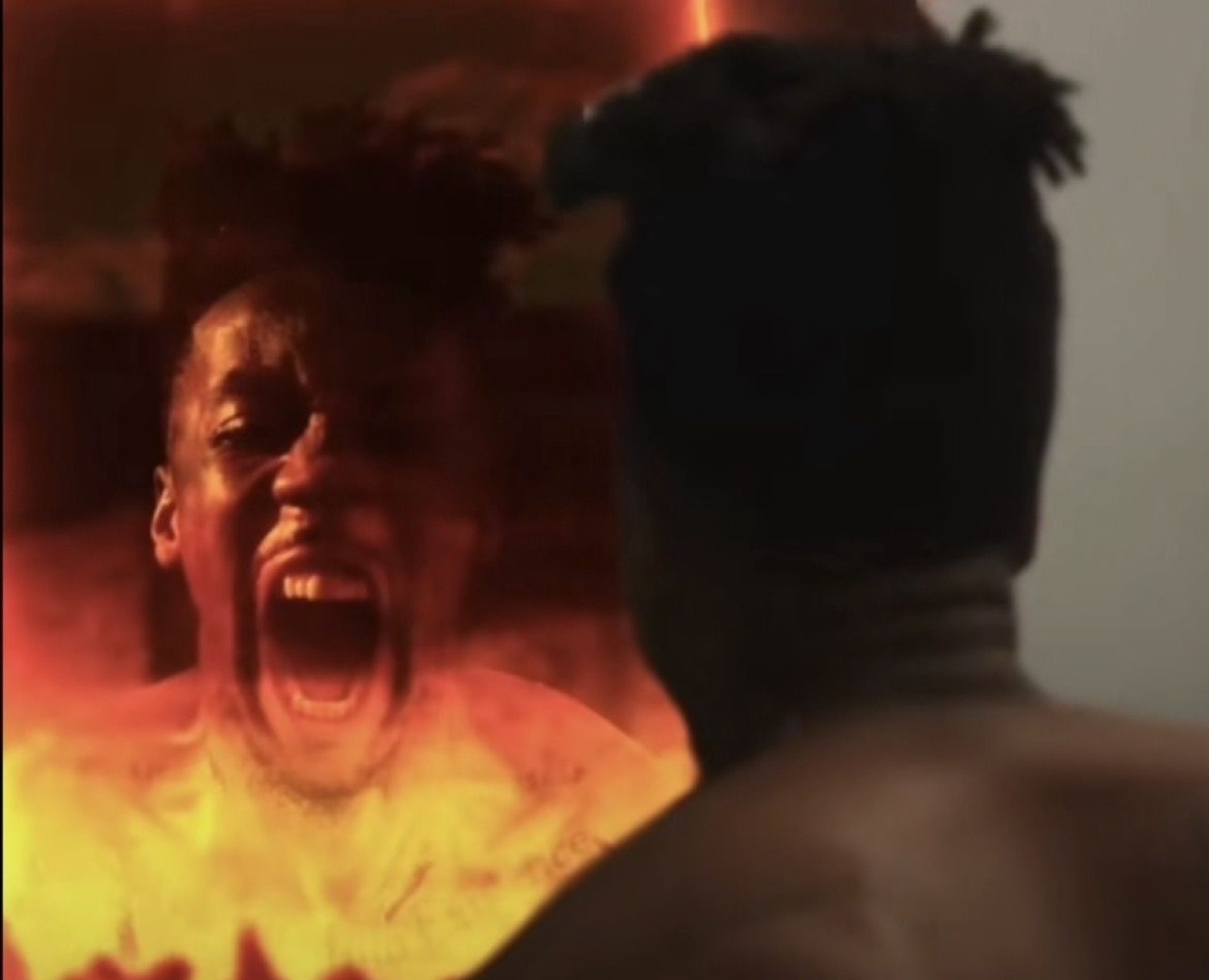 A man engulfed in orange flames screaming intensely while another figure watches