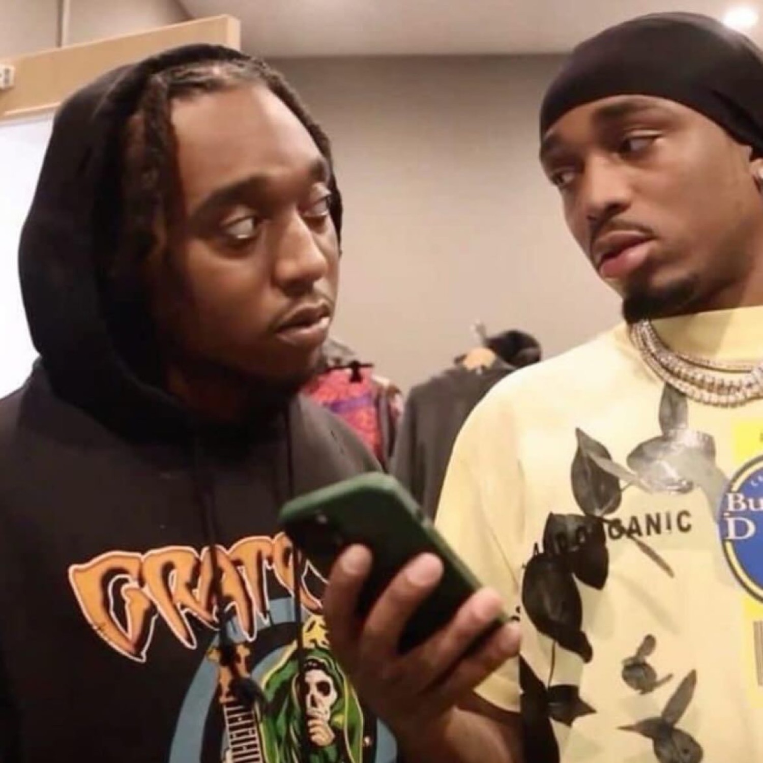 Two rappers hunched over one phone, both throwing serious side-eye at the screen