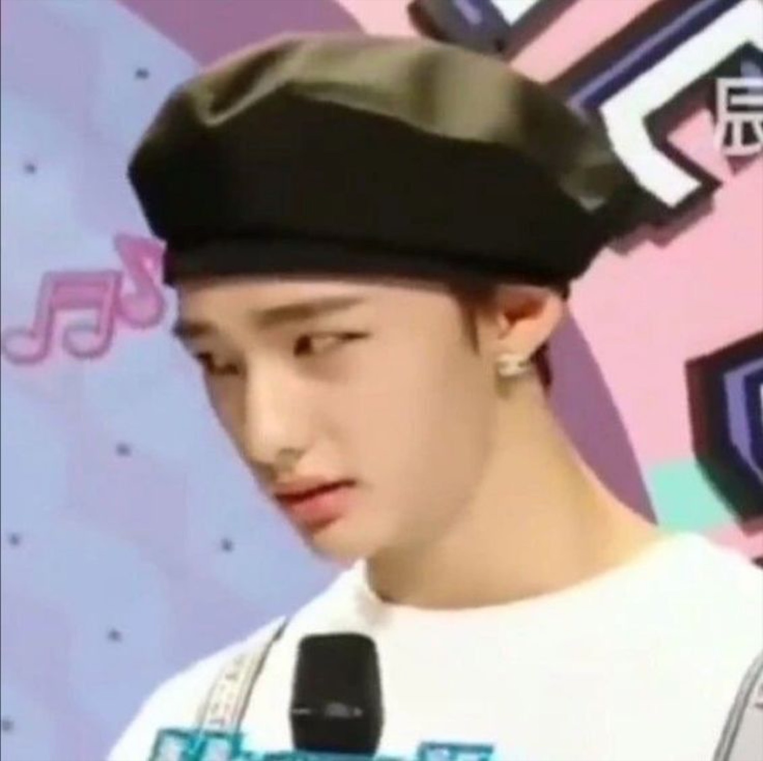 K-pop style guy in a black beret giving a slow side-eye at a colorful music event