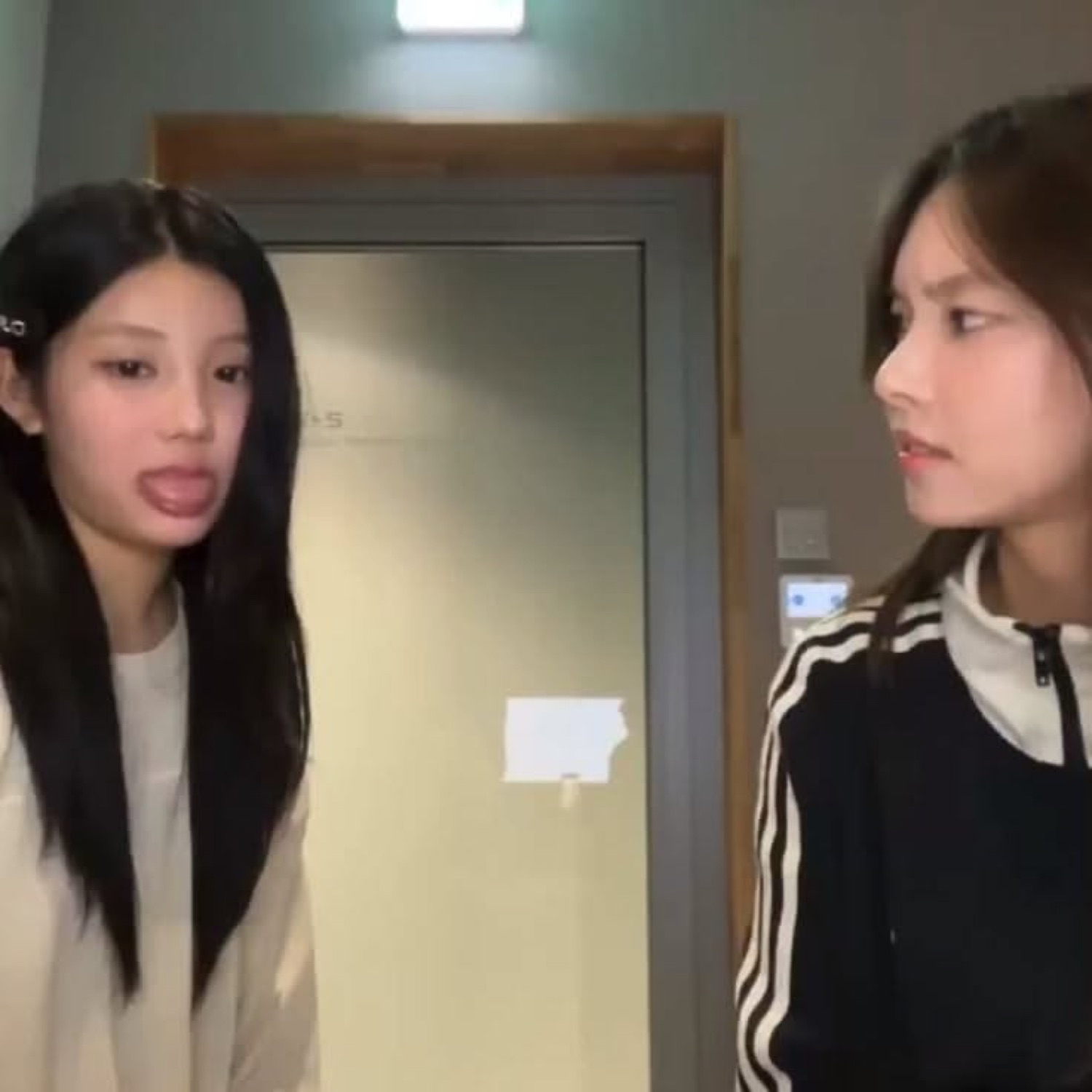 Two young women in a hallway, one sticking her tongue out at the other who side-eyes her
