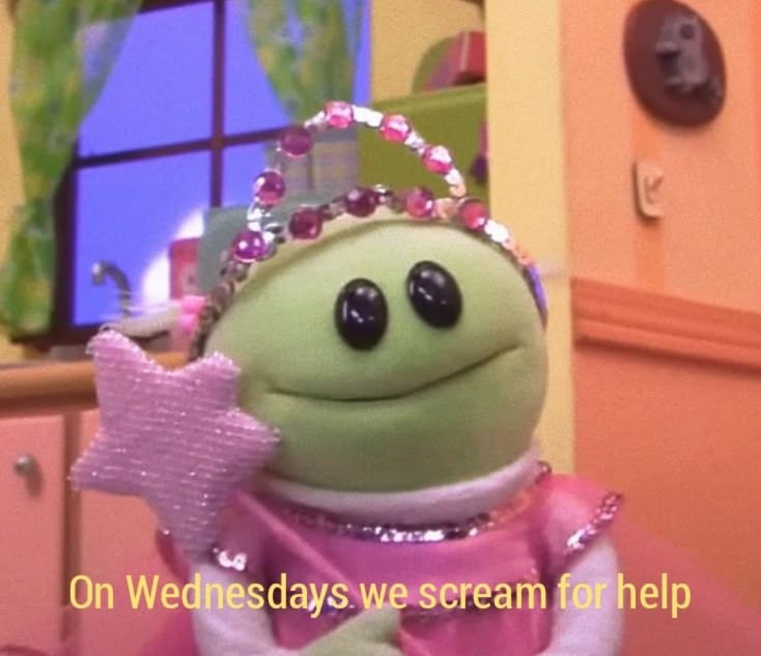 Green frog puppet in a sparkly princess costume captioned 'On Wednesdays we scream for help'