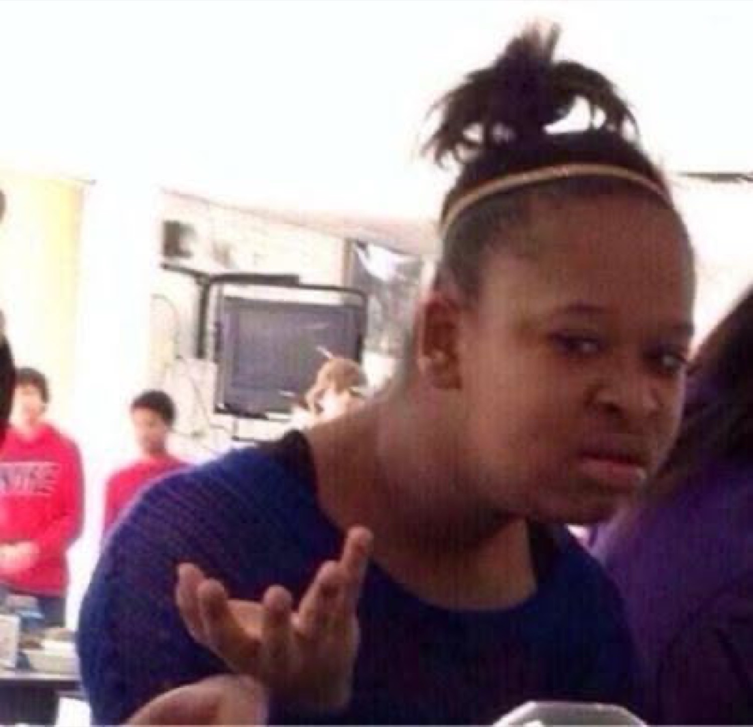 Girl in a classroom raising a hand with a confused, unimpressed grimace