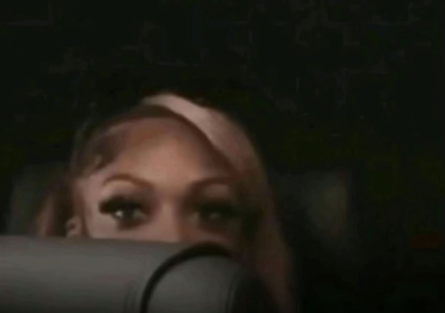 Woman peeking over a car seat in the dark with wary narrowed eyes