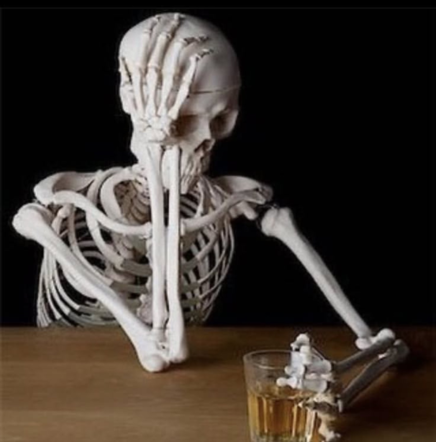 Skeleton facepalming at a table next to a glass of whiskey