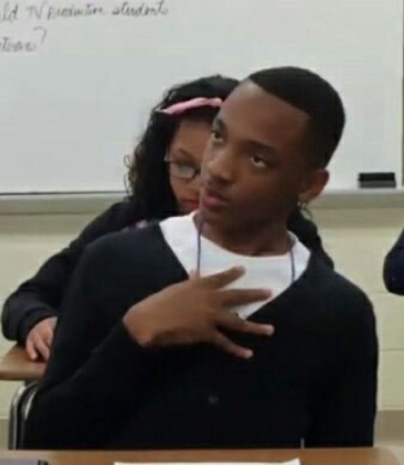 Student in a classroom looking to the side with narrowed eyes while a classmate reaches around him