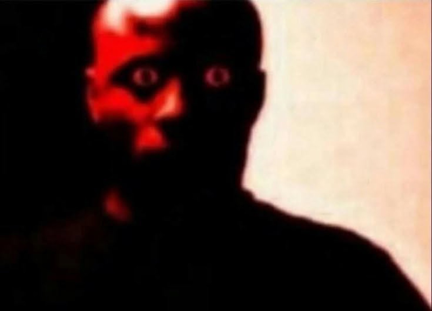 Shadowy red-lit face with glowing eyes staring straight through you