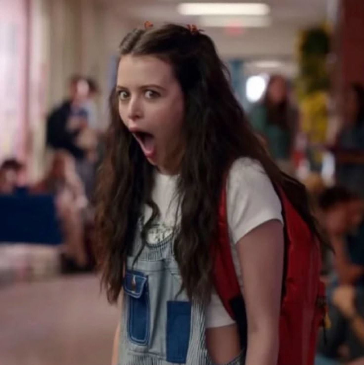 Girl in overalls in a school hallway gasping with a dropped jaw