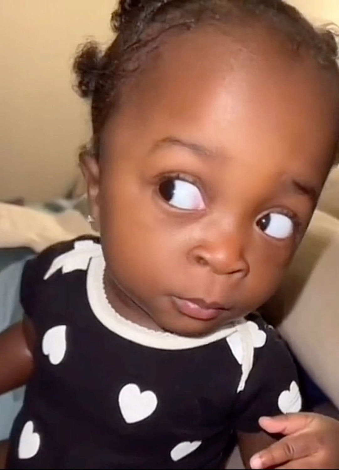 Baby in a heart-print onesie cutting a slow, suspicious side-eye