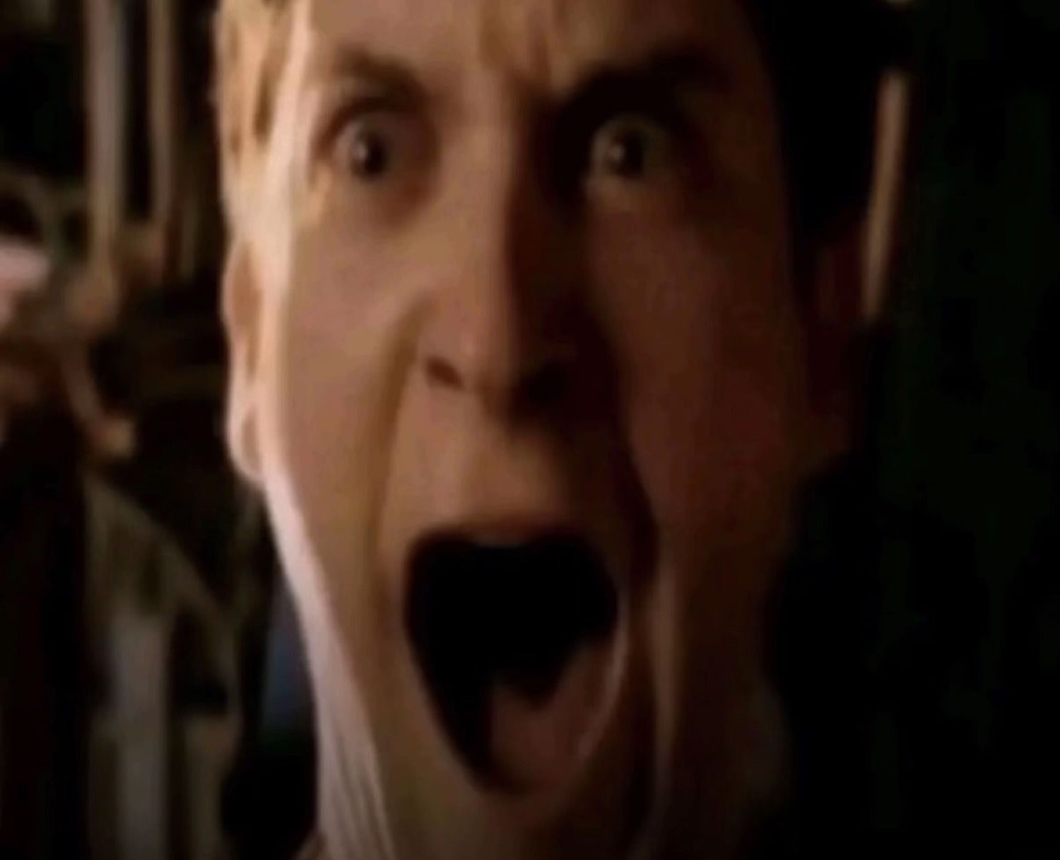 Man screaming with wide eyes and his mouth stretched open in a dim room
