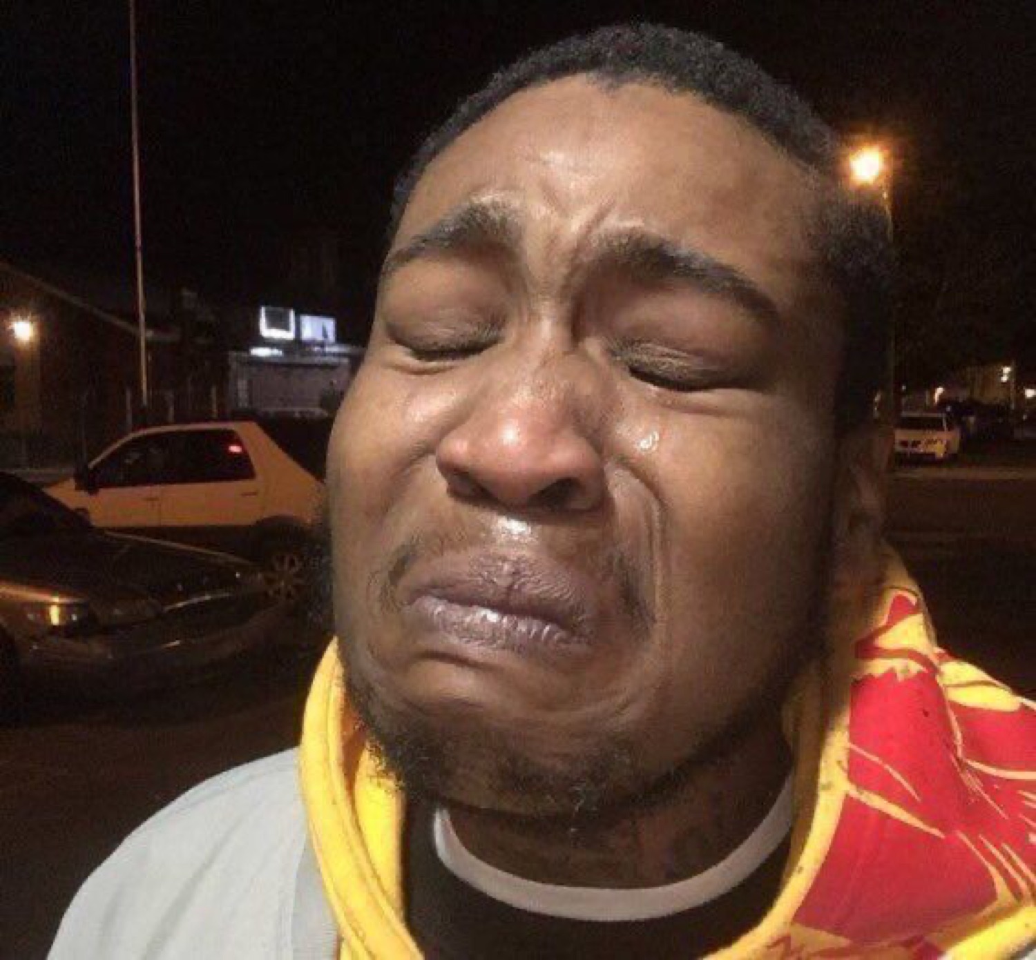 Man outside at night with his eyes squeezed shut, tears running down a crying face