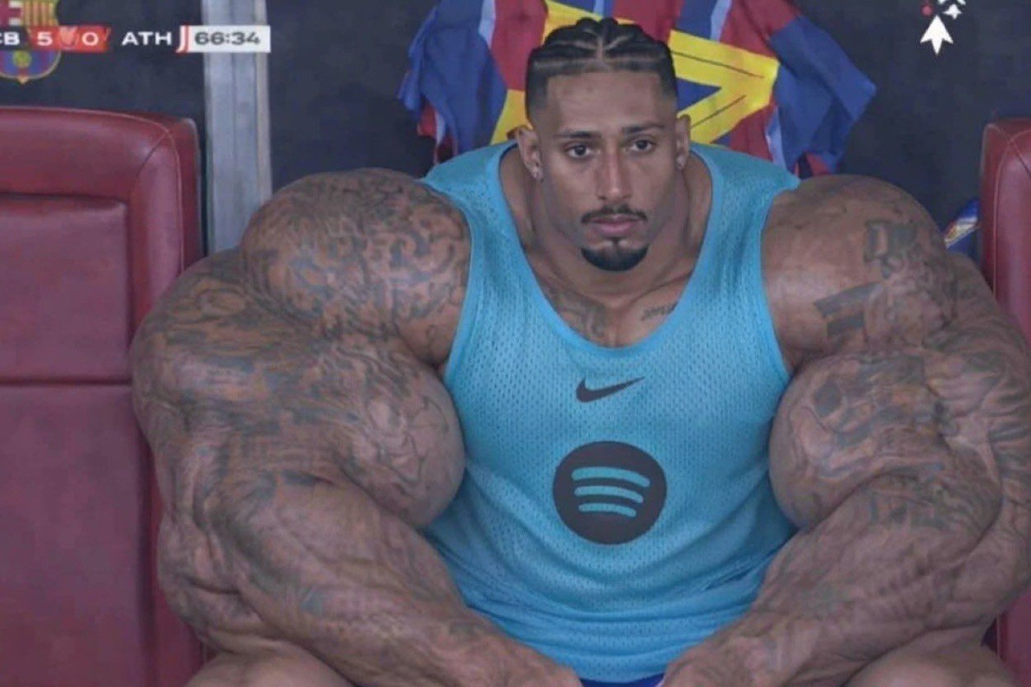 Guy edited with gigantic muscles sitting in a Nike tank top